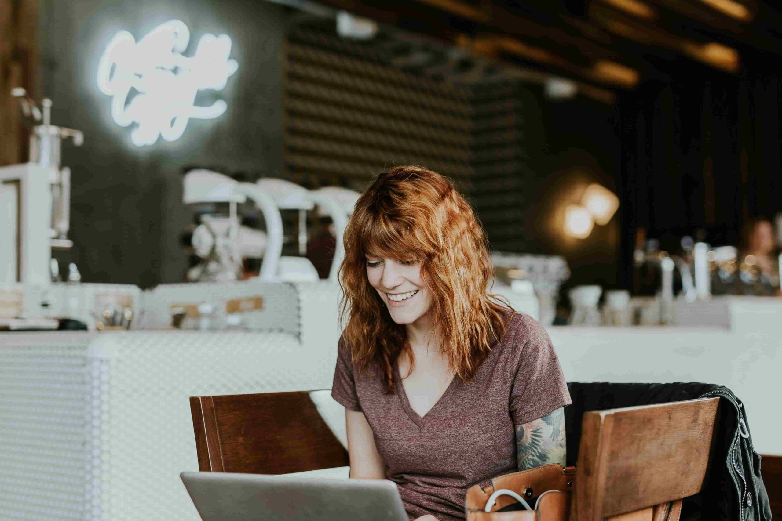 Smiling woman working on a laptop in a modern café, representing flexibility and productivity through HR outsourcing solutions for small businesses.