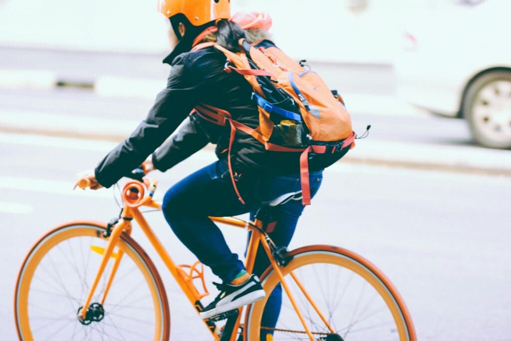 A cyclist on a bright orange bike, navigating through a bustling city street, representing proactive HR strategies. This image symbolizes the dynamic and agile approach necessary for maintaining compliance and efficiency in the ever-changing landscape of employment law.
