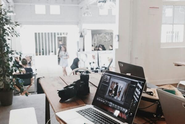 A modern workspace with laptops and a camera on a wooden table, representing collaboration and creativity as a competitive advantage.