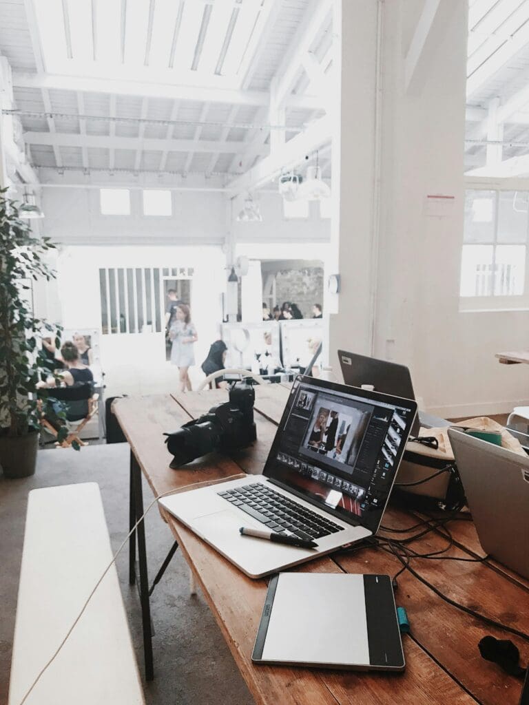 A modern workspace with laptops and a camera on a wooden table, representing collaboration and creativity as a competitive advantage.