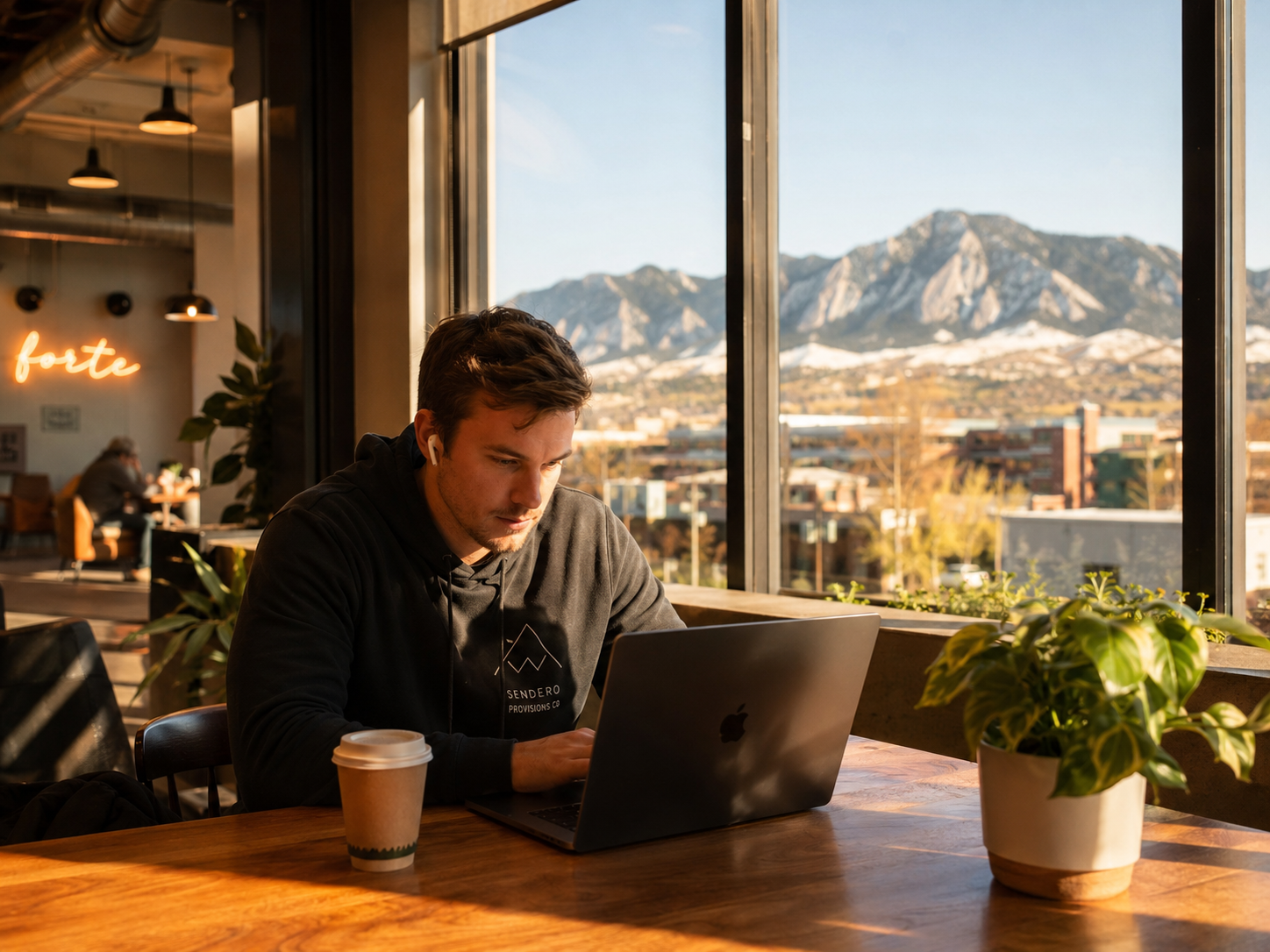 A young founder working on a laptop in a warm Colorado coworking space with mountains in the window